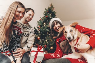 메리 크리스마스와 새해 복 많이 받으세요. 크리스마스 트리 조명에서 선물을 교환하는 축제 스웨터를 입은 세련된 힙스터 가족. 즐거운 휴일 보내세요. 재미있는 감정적 순간들