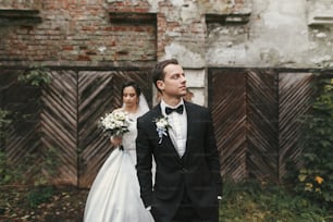 lindo casal de casamento posando no prédio antigo. noiva elegante com buquê e noivo abraçando na rua da cidade europeia no outono. momento sensual romântico dos recém-casados