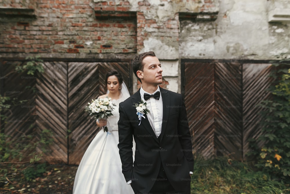 gorgeous wedding couple posing  at old building. stylish bride with bouquet and  groom embracing  in european city street in autumn time. romantic sensual moment of newlyweds