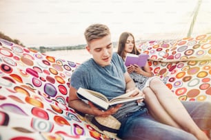 happy hipster couple reading books and relaxing in hammock in sunset light on the beach, summer vacation. stylish hipster family holding books and resting on holidays  in warm summer evening
