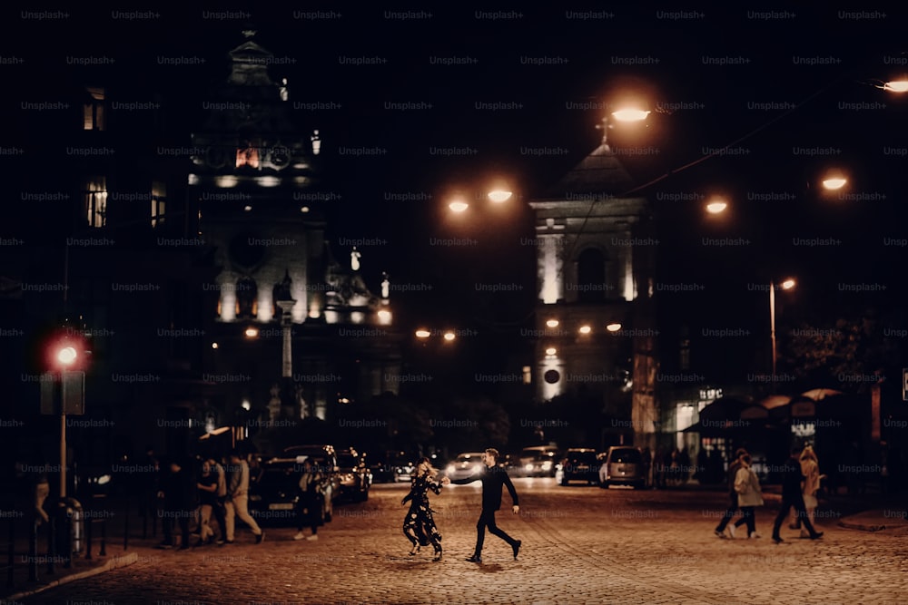 lovers running through empty road in the evening city street. stylish couple in love having fun and holding hands in city lights. modern woman and man romantic french atmospheric moment