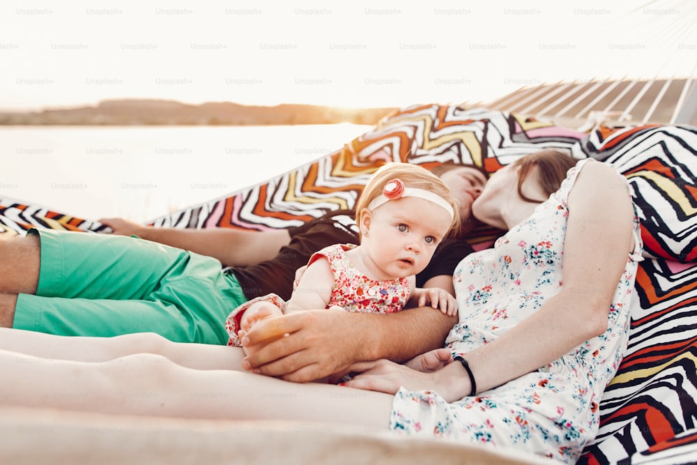 Adorable baby girl  shocked face, lying with her happy father and mother, young hipster couple relaxing with daughter in  a hammock, cute scared baby