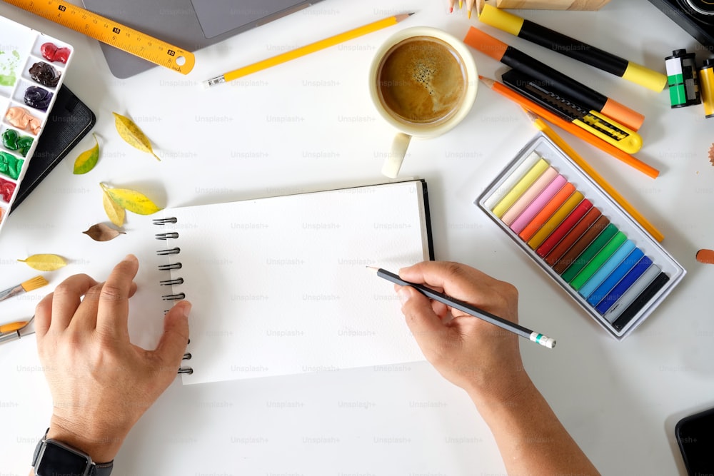 Künstlerhände skizzieren auf leerem Notizbuch auf kreativem Arbeitsbereich.