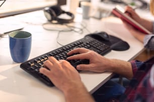Detail of business people working in an office; man typing on a keyboard, woman taking notes, writing in a planner. Selective focus on the index finger and the keyboard