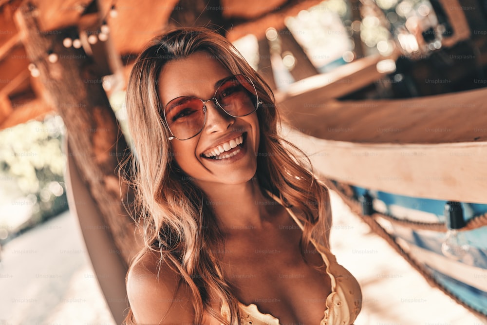 Attractive young woman smiling and looking away while standing on the beach near the bar counter