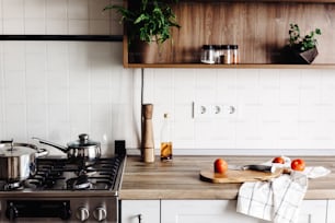 Cooking on Modern Kitchen  in scandinavian style. stylish kitchen interior with modern furniture and stainless steel appliances. wooden countertop, steel stove, board,knife and spices, tomatoes