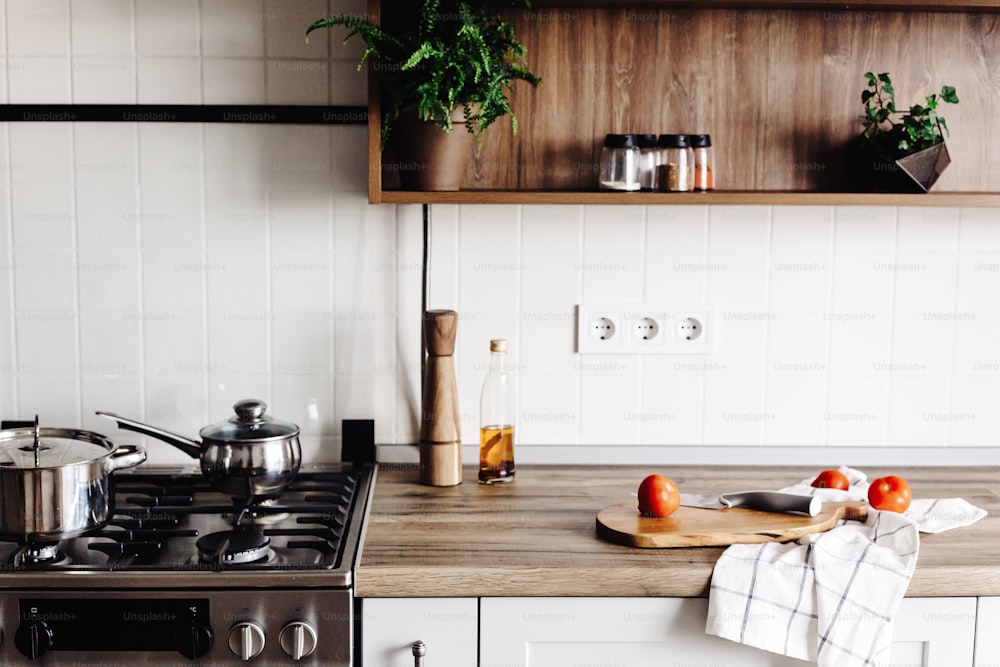 Cocina en cocina moderna de estilo escandinavo. Elegante interior de cocina con muebles modernos y electrodomésticos de acero inoxidable. encimera de madera, estufa de acero, tablero, cuchillo y especias, tomates