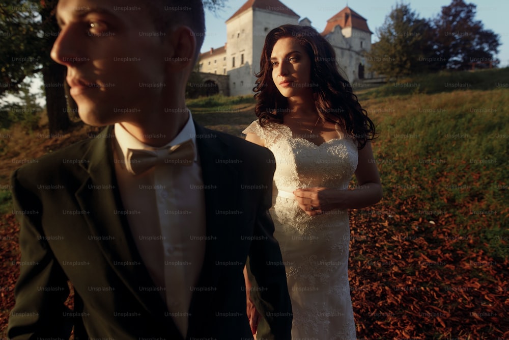 gorgeous bride and stylish groom posing in soft light at sunset near castle. sensual moment of beautiful wedding couple outdoors