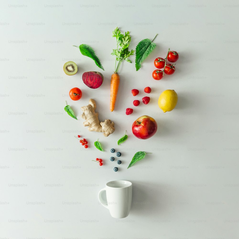 Kreatives Food-Layout mit Obst, Gemüse und Blättern auf hellem Marmortischhintergrund mit Teetasse. Minimales gesundes Getränkekonzept. Flache Liege.