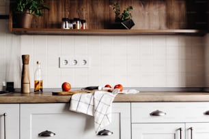 칼, 토마토, 현대적인 주방 조리대에 올리브 오일이 있는 나무 보드와 향신료와 식물이 있는 선반. 음식 요리. 스칸디나비아 스타일의 세련된 주방 인테리어 디자인, 철강 가전 제품