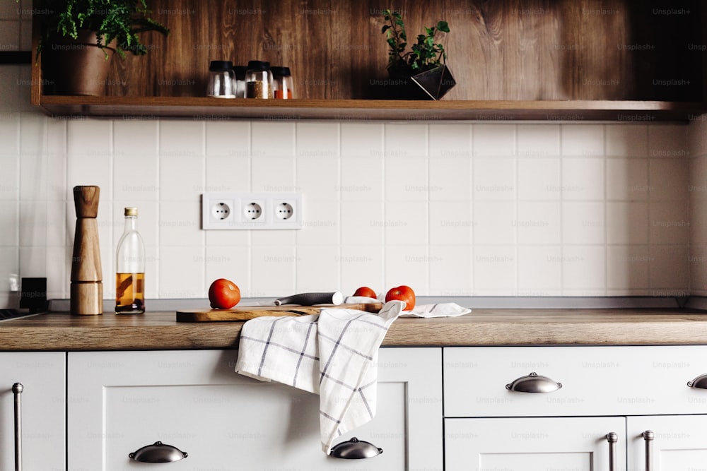 Planche en bois avec couteau, tomates, huile d’olive sur le comptoir de cuisine moderne et étagère avec des épices et des plantes. cuisson des aliments. Design d’intérieur de cuisine élégant dans un style scandinave, appareils électroménagers en acier