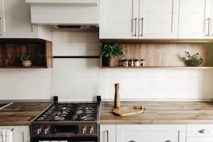 Diseño de cocina moderna en estilo escandinavo. Elegante interior de cocina de color gris claro con muebles modernos y electrodomésticos de acero inoxidable. encimera de madera, estufa de acero, tablero, cuchillo y especias