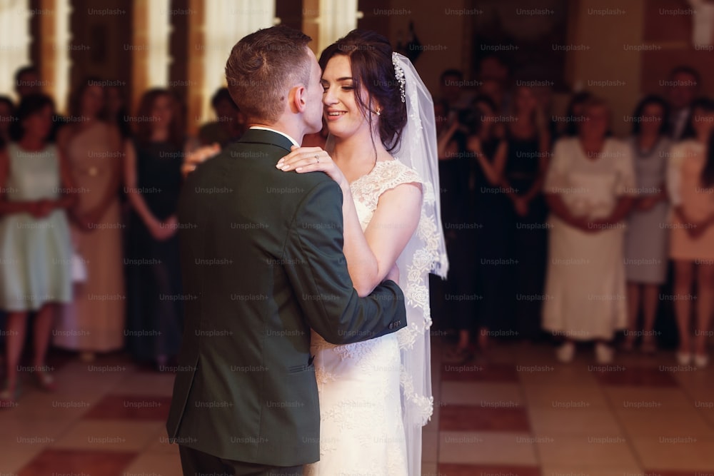 Romantic newlywed couple hugging, handsome groom and beautiful happy bride first dance while holding hands at restaurant wedding reception, beautiful lighting