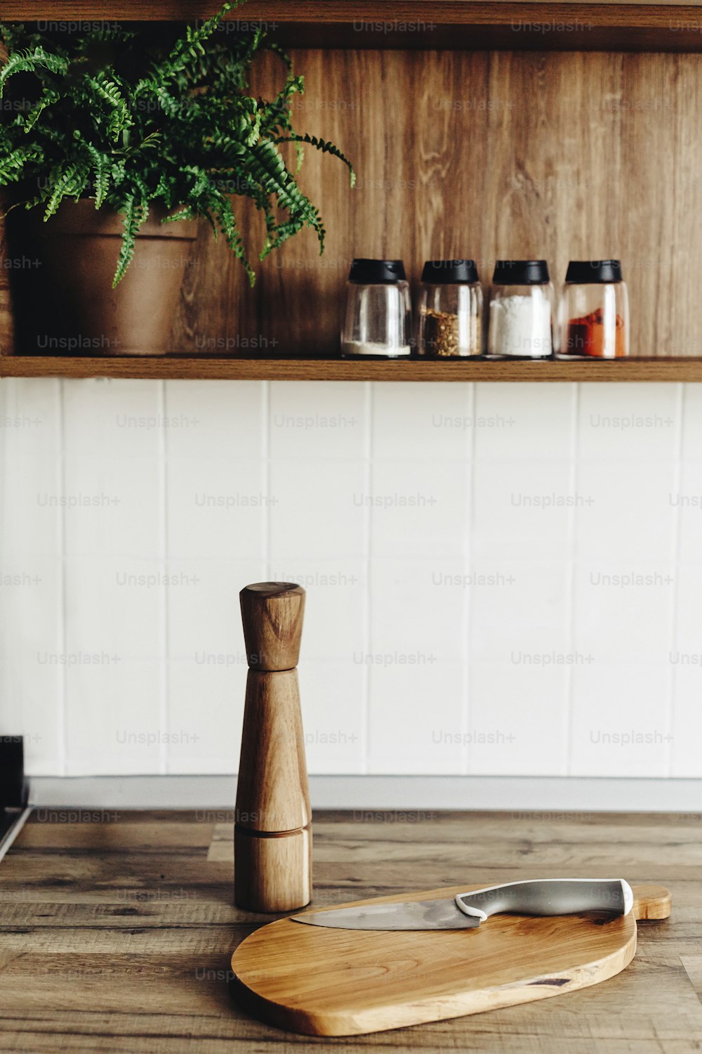 ナイフ付きの木の板、モダンなキッチンのカウンタートップに木製のペッパーミル、スパイスや植物が置かれた棚。食べ物を調理する。スカンジナビアスタイルのスタイリッシュなキッチンインテリアデザイン