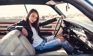 Attractive young woman is sitting in green retro car on the beach. Vintage classic car.