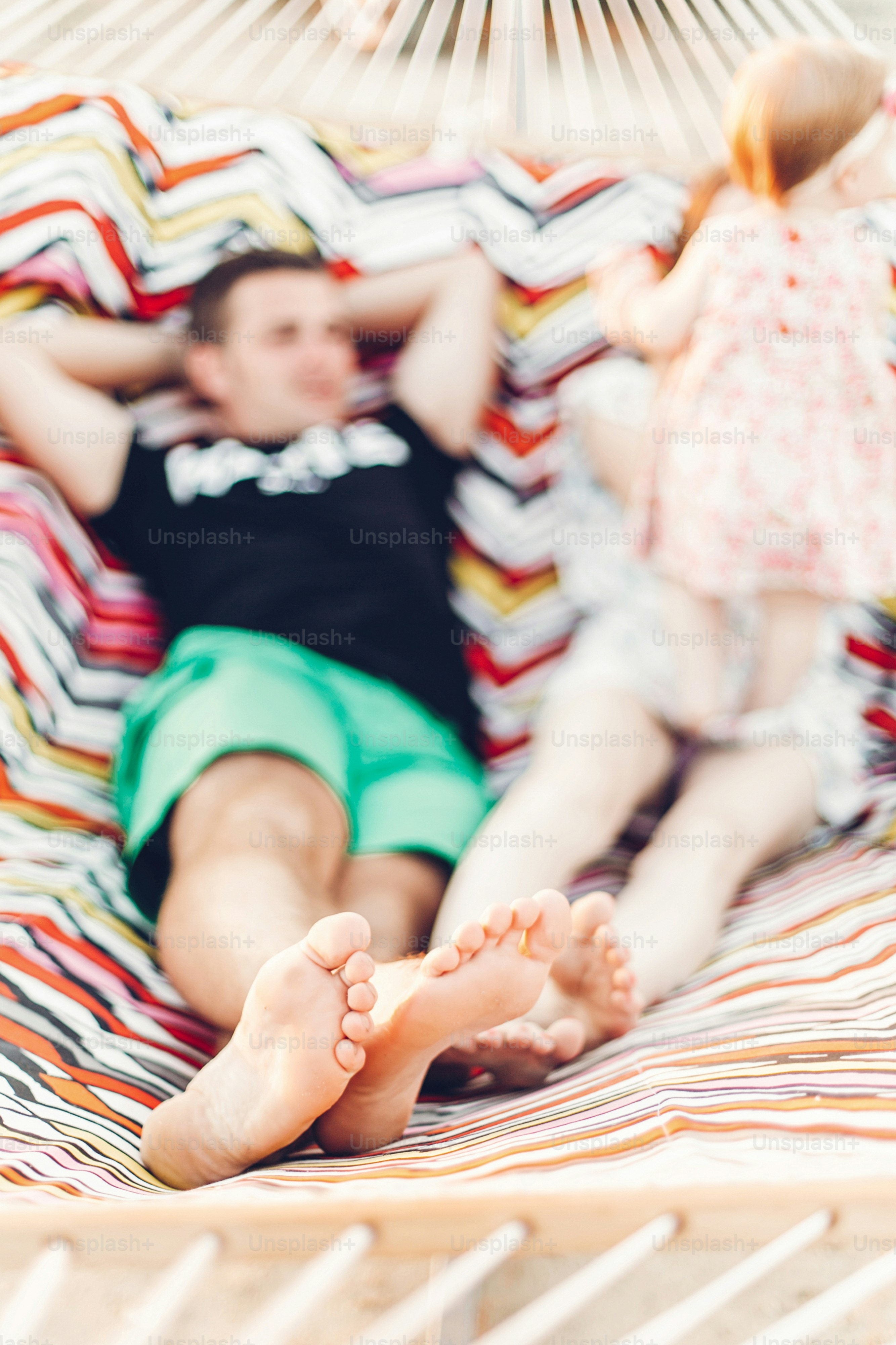 legs of a happy stylish family playing with cute daughter, relaxing in hammock on summer vacation in evening sun light on the beach. hipster couple with child resting in sunset. space for text