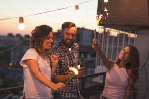 Group of young friends having fun at a rooftop party, singing, dancing and waving with sparklers