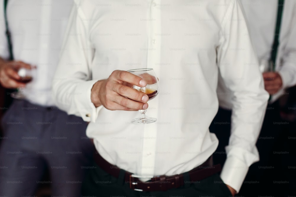 stylish groom with groomsmen holding whiskey in glass in the morning before wedding preparation. luxury group of friends. confident business man