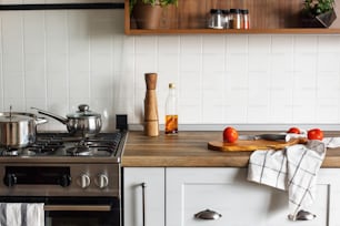 wooden board with knife, tomatoes, olive oil on modern kitchen countertop and steel stove with saucepan. cooking food. Stylish gray kitchen interior design in scandinavian style