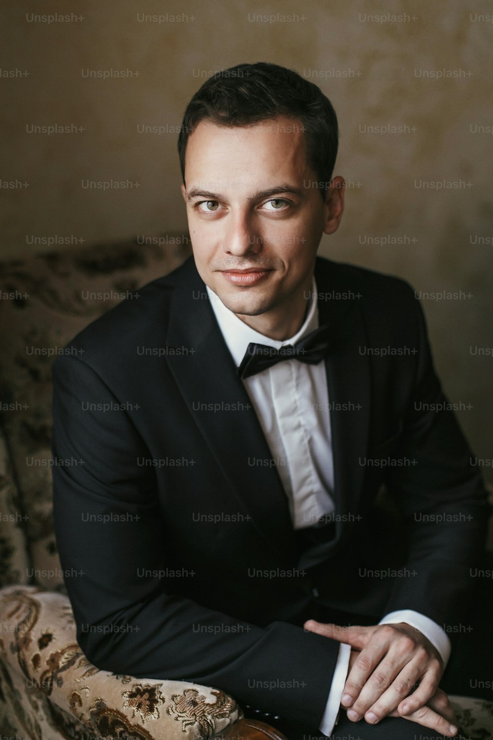 handsome Groom portrait in the morning in the room. happy man in suit with bow tie smiling, sitting in chair at window light in hotel. preparation for wedding day