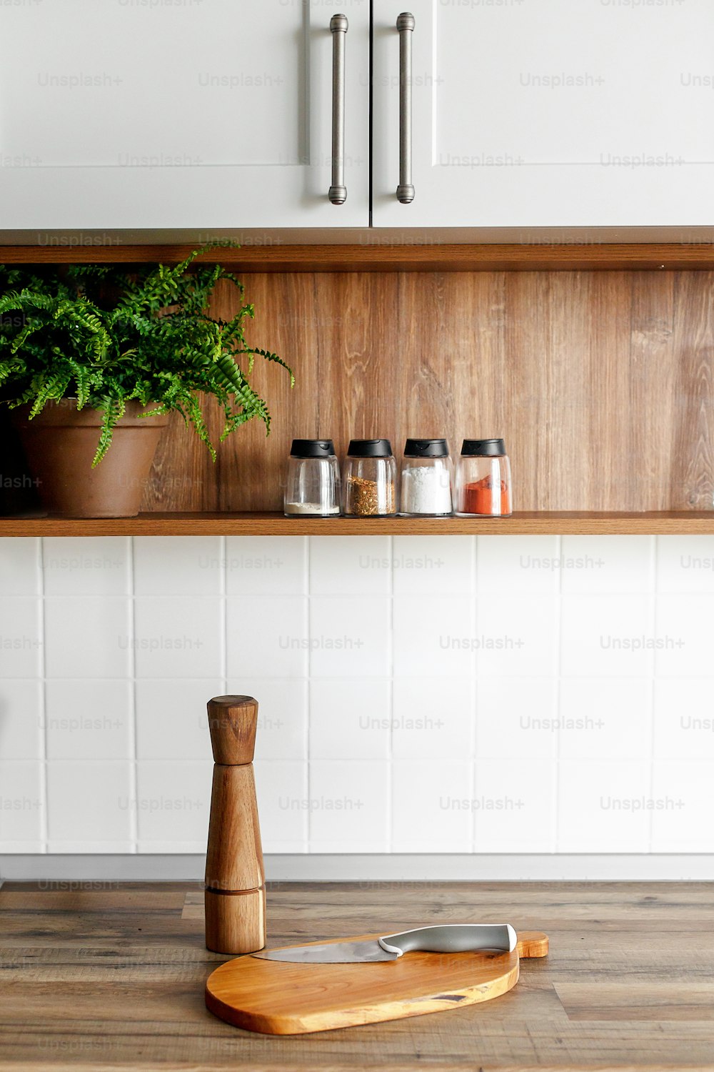 wooden board with pepper mill and knife on modern kitchen countertop and shelves with food ingredients and spices in glass jars. Stylish gray kitchen interior  design in scandinavian style