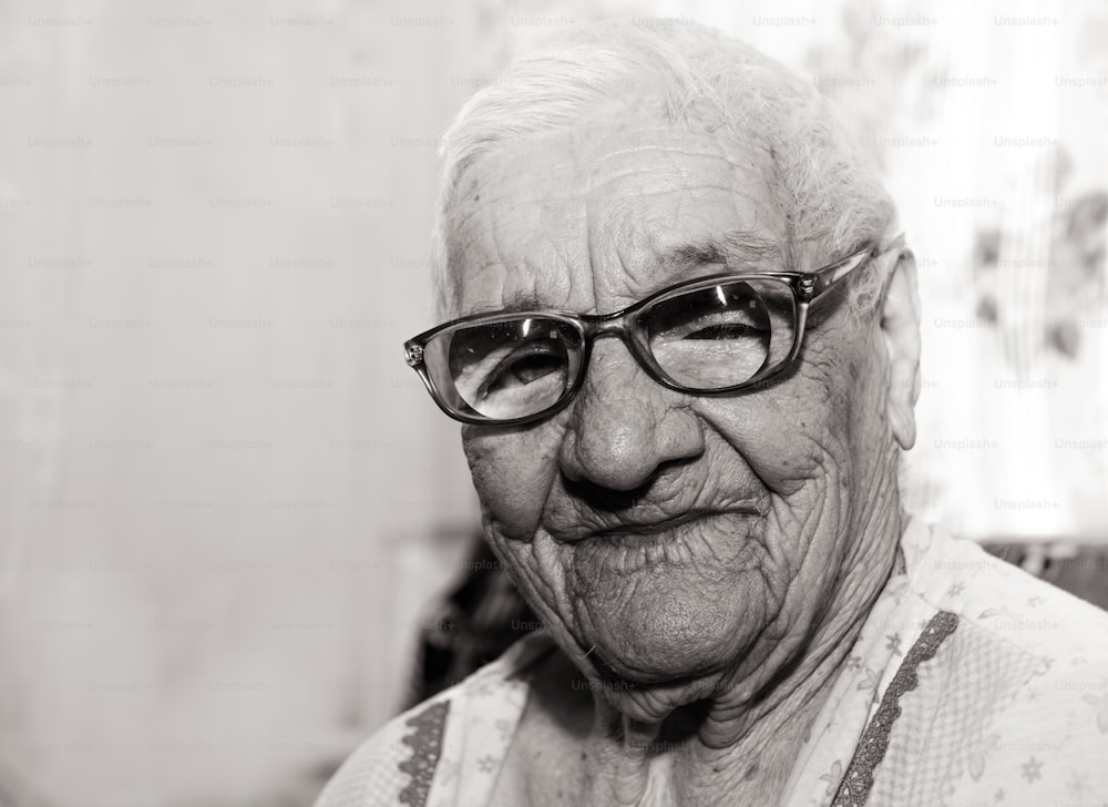 Schwarz-Weiß-Porträt einer alten faltigen hundertjährigen Frau. Eine lächelnde Großmutter mit großer Brille. Alter, Freundlichkeit und Weisheit