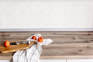 tábua de madeira com faca, tomates, toalha na bancada da cozinha moderna. imagem simples, conceito de culinária. cozinhar alimentos. Design de interiores de cozinha elegante em estilo escandinavo