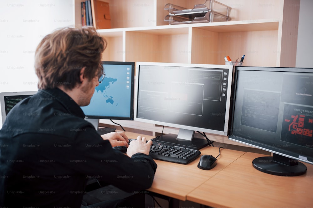 Programador masculino que trabaja en una computadora de escritorio con muchos monitores en la oficina en una empresa de desarrollo de software. Tecnologías de diseño, programación y codificación de sitios web.