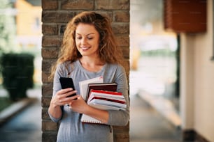 Female student using smartphone and holding books.
