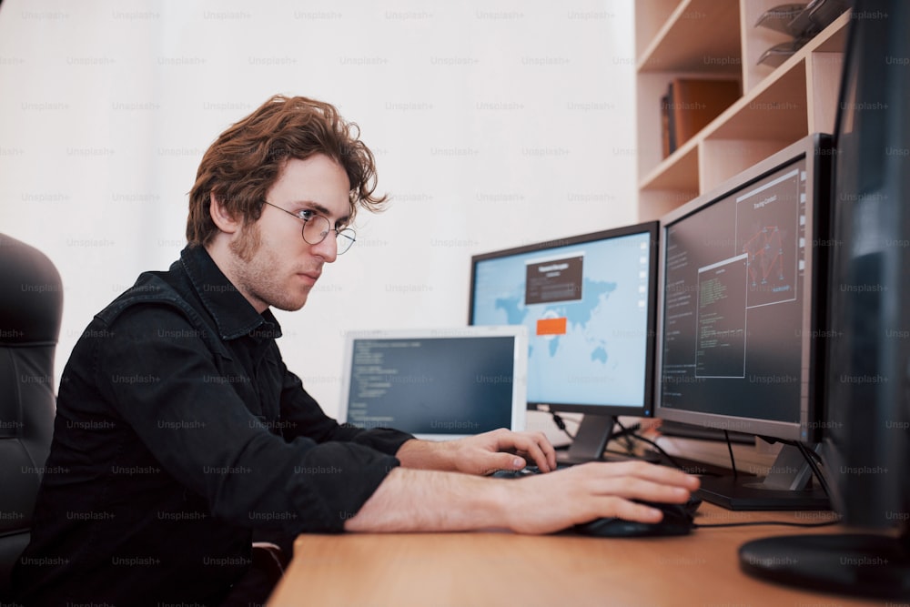 Male programmer working on desktop computer with many monitors at office in software develop company. Website design programming and coding technologies.