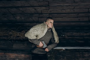 Strong, angry viking warrior with axe before battle at war, ancient scandinavian warrior cosplay, thor costume, northern lumberjack costume, confident facial expression of  man near wooden building