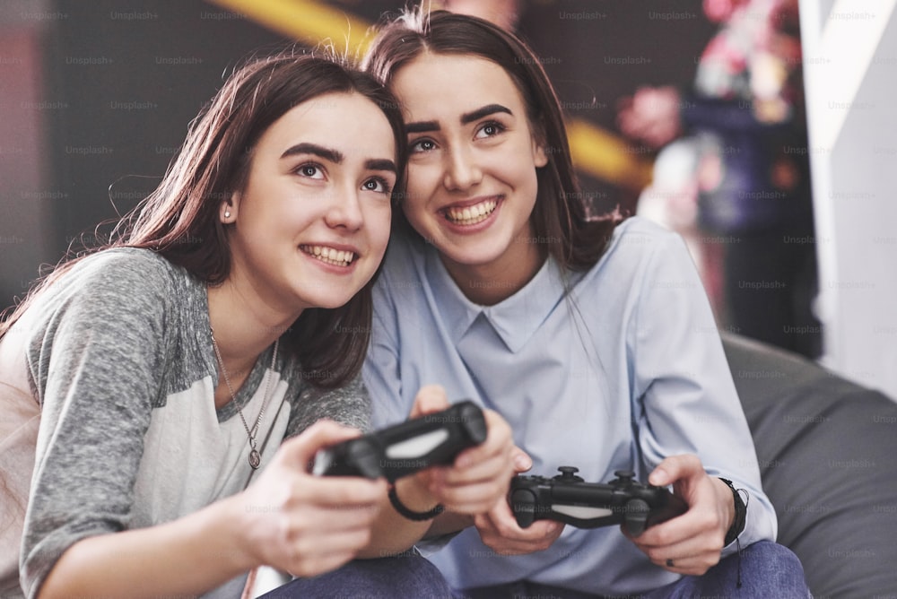Twin sister sisters play on the console. Girls hold joysticks in their hands and have fun.
