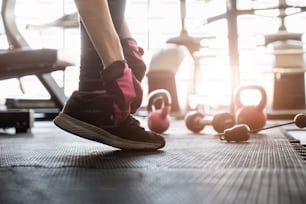 Close up front view of woman's hands tying shoelaces on sneakers in the gym.