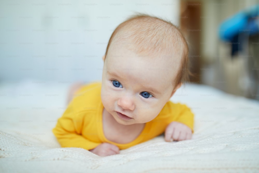 Adorabile bambina di due mesi che si rilassa in camera da letto su una coperta lavorata a maglia in una mattina di sole. Neonato che fa il tempo della pancia