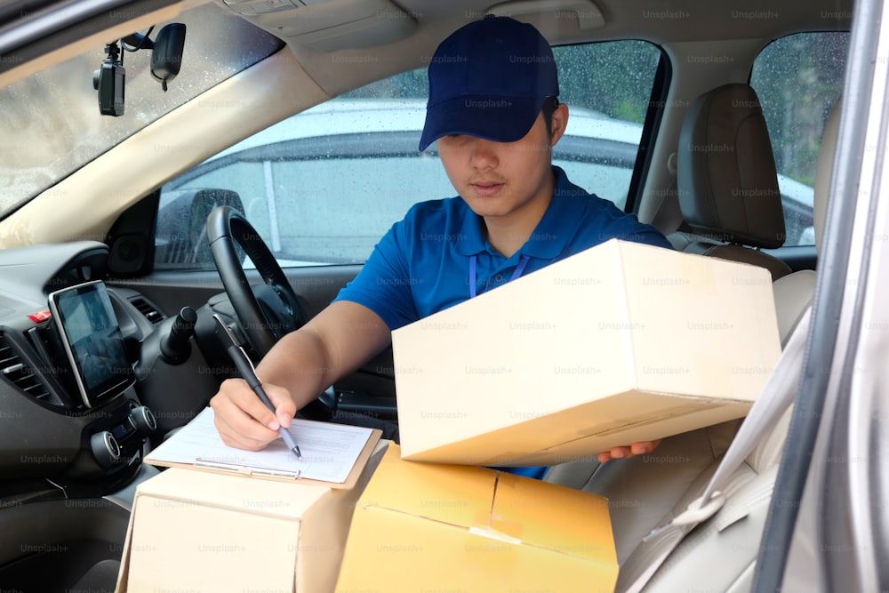 Retrato de um entregador asiático homem escrevendo em uma prancheta enquanto sentado em uma van de entrega