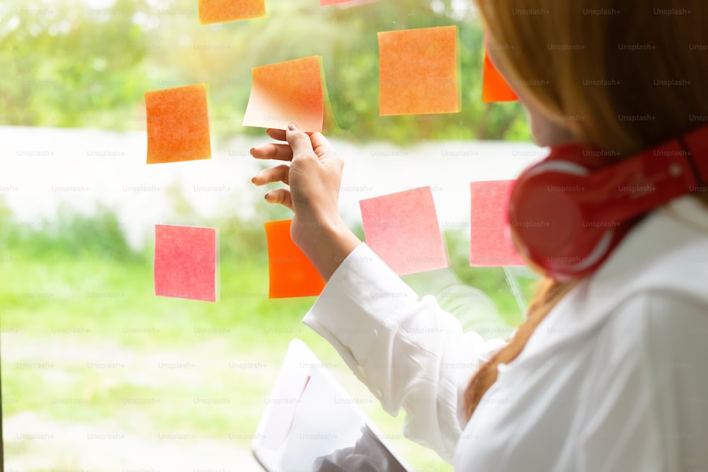 Woman sticking adhesive notes on glass wall in office with vintage tone.