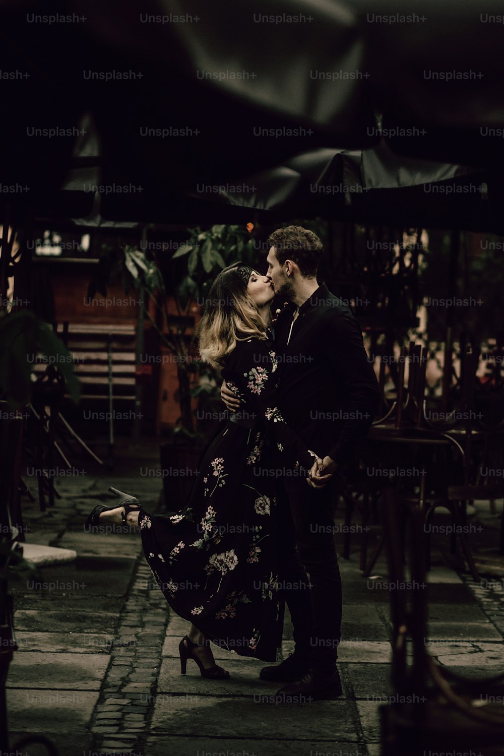 Coppia felice che si bacia all'aperto vicino agli ombrelli in un ristorante a Parigi, fidanzato elegante e fidanzata si abbracciano in vacanza, concetto di passione