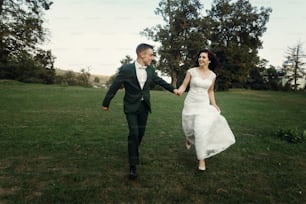 stylish luxury bride and groom having fun running together in evening sunny light near old castle. emotional moment of beautiful wedding couple outdoors