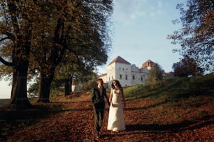 casal de luxo andando de mãos dadas na luz suave da noite ao pôr do sol perto do castelo. momento romântico sensual de noiva linda linda e noivo elegante ao ar livre