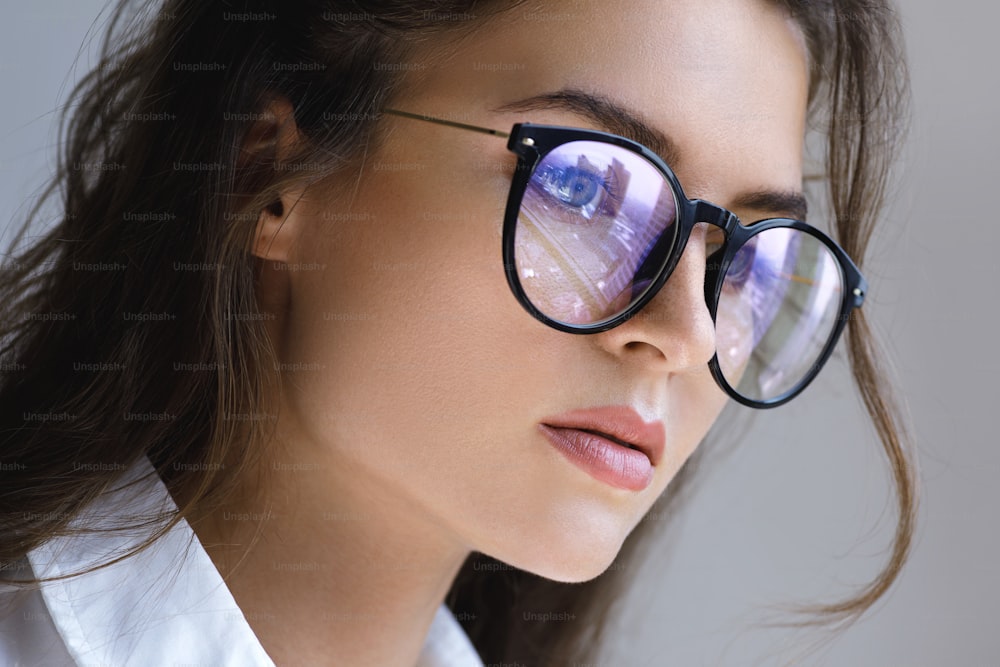 Thoughtful businesswoman thinking about future. Closeup portrait of young woman with a reflection of modern city inside eyeglasses.