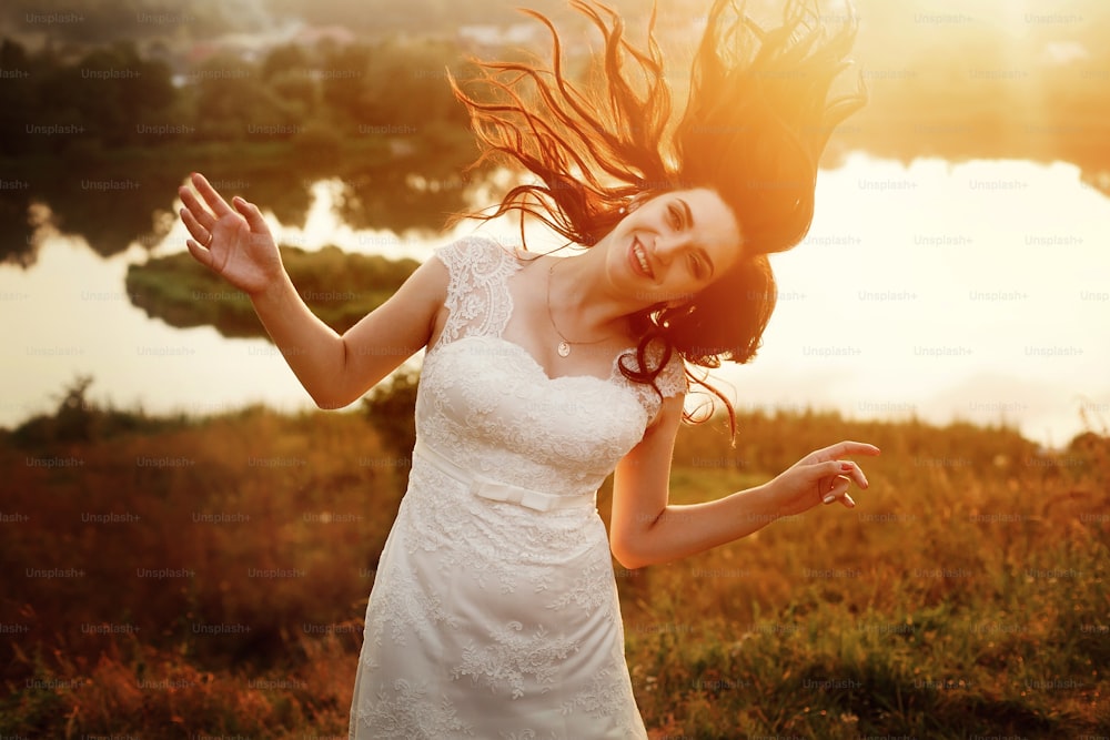 happy gorgeous bride smiling and having fun jumping in the evening warm sunlight. sensual emotional moment of luxury wedding couple in amazing sunset