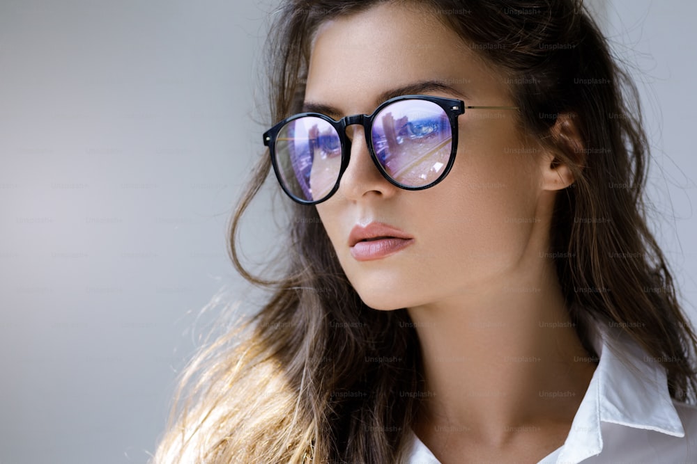 Thoughtful businesswoman thinking about future. Closeup portrait of young woman with a reflection of modern city inside eyeglasses.