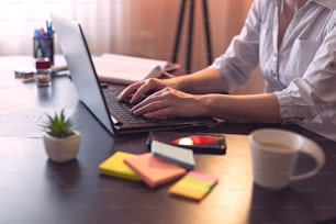 Detail of a businesswoman's hands typing on a laptop computer keyboard. Selective focus on the keyboard and the fingers