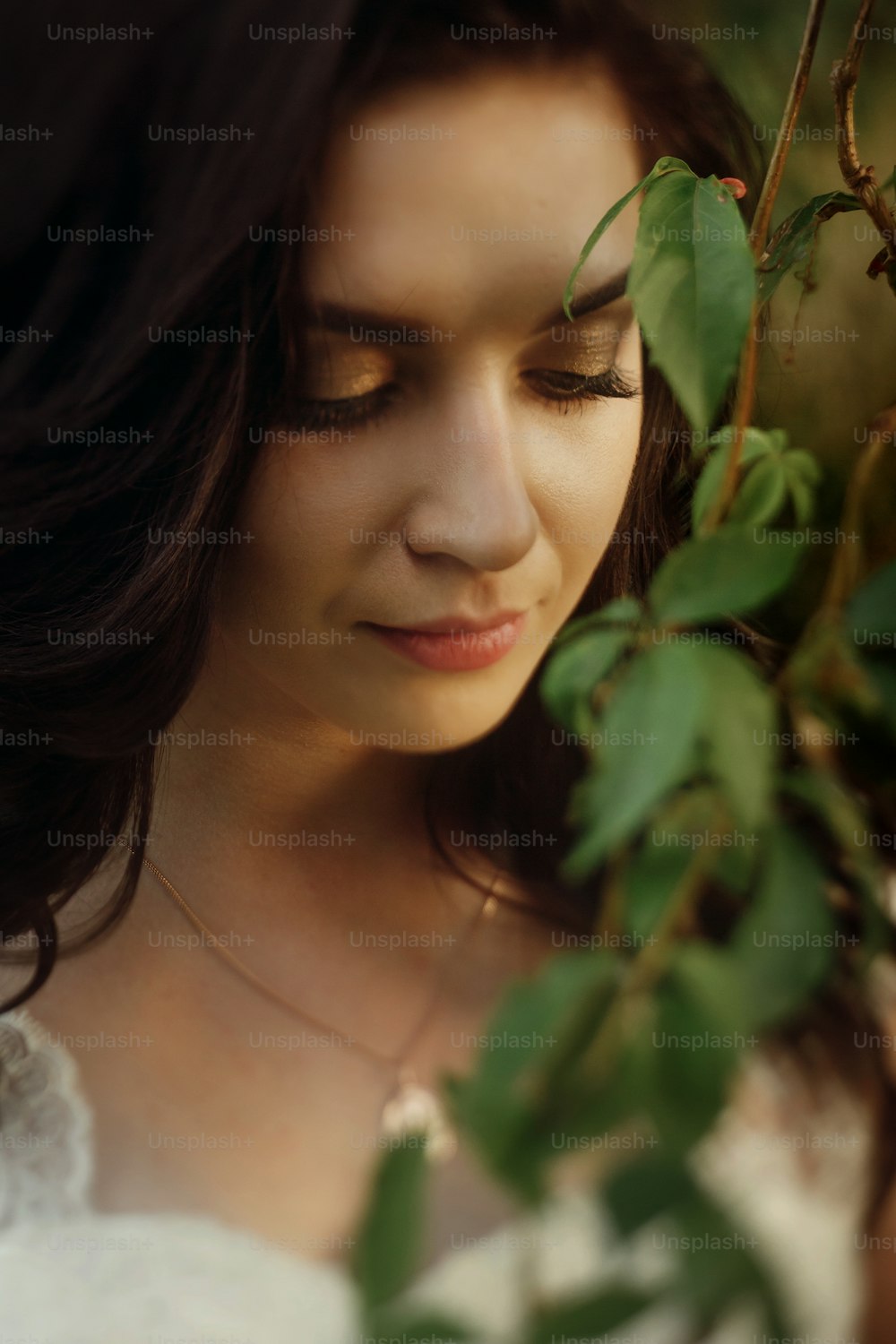 Close-up of beautiful female bride face, gorgeous sensual brunette woman looking down near tree branch with leaves, portrait