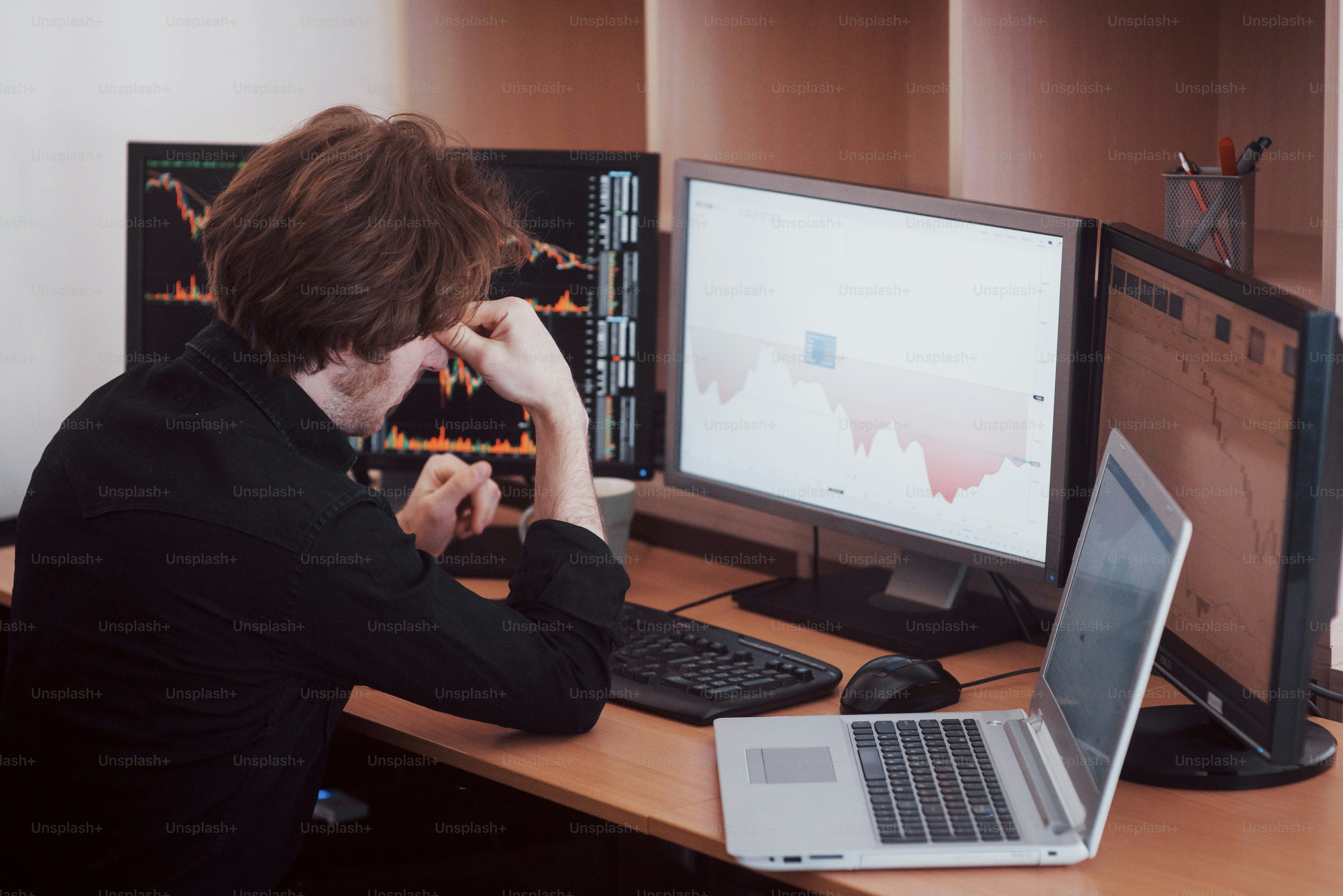 Hari yang menegangkan di kantor. Pengusaha muda berpegangan tangan di wajahnya sambil duduk di meja di kantor kreatif. Perdagangan Bursa Efek Konsep Grafis Keuangan Forex.