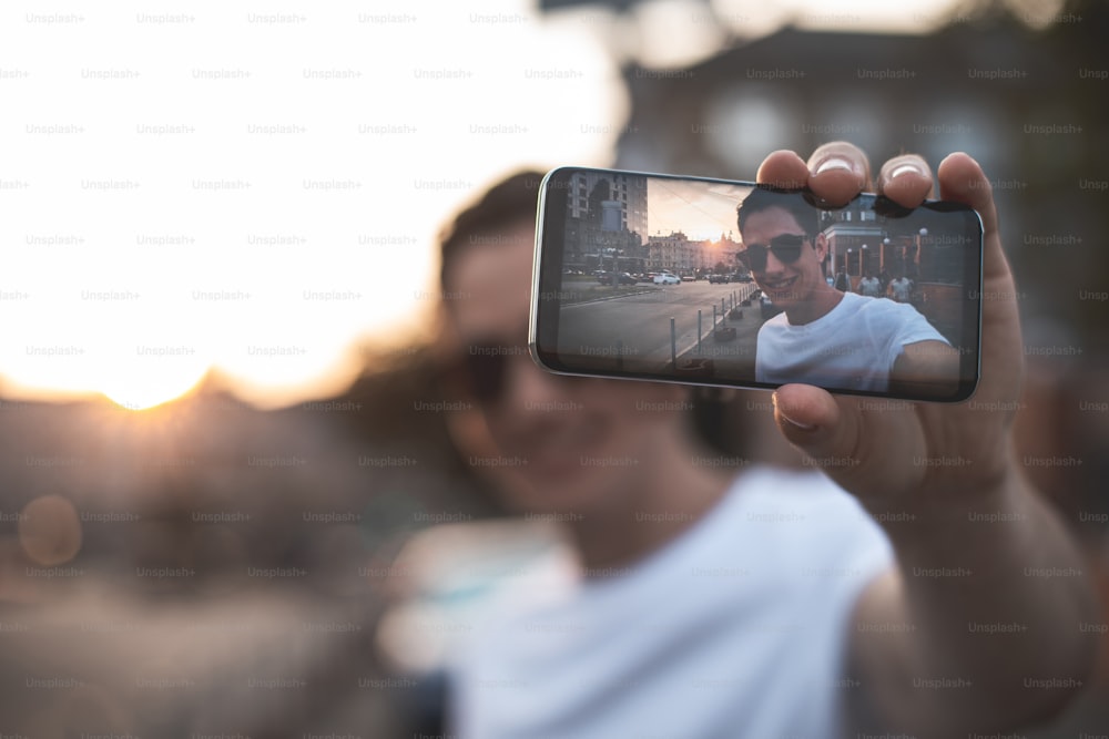 Focus on male hand holding smartphone outdoors. He is standing and photographing himself at sunset. Copy space in left side