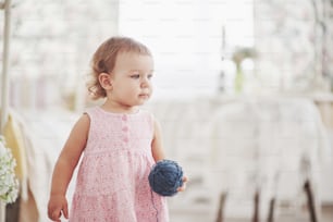 Childhood concept. Baby girl in cute dress play with colored thread. White vintage childroom.