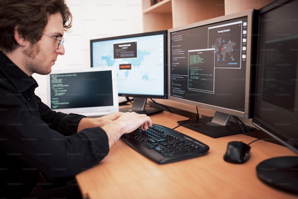 ソフトウェア開発会社のオフィスで多くのモニターを備えたデスクトップコンピューターで作業している男性プログラマー。Webサイトのデザイン、プログラミング、コーディング技術。