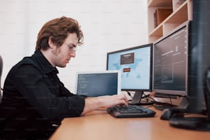 The young dangerous hacker breaks down government services by downloading sensitive data and activating viruses. A man uses a laptop computer with many monitors.