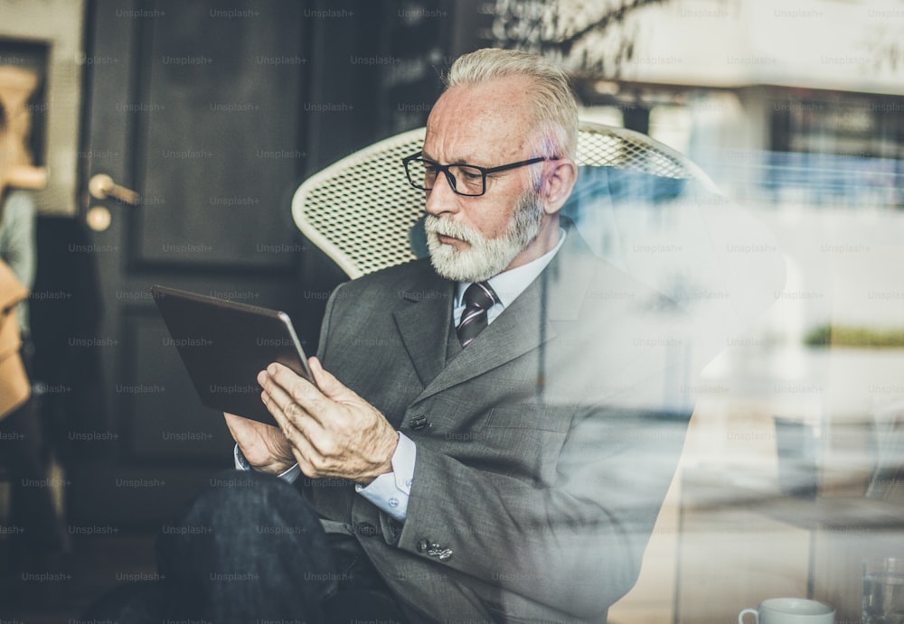 Hombre de negocios senior trabajando en una tableta digital en una cafetería.